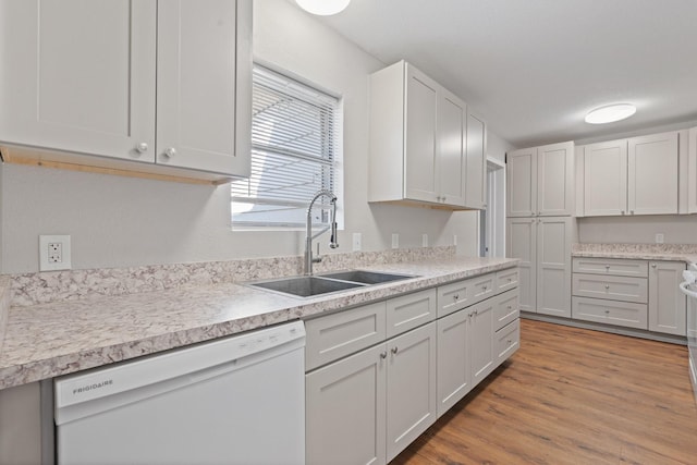 kitchen with light wood finished floors, white dishwasher, a sink, light countertops, and white cabinetry