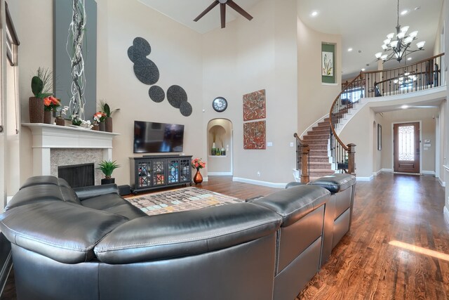 living room with stairway, ceiling fan with notable chandelier, arched walkways, a fireplace, and wood finished floors