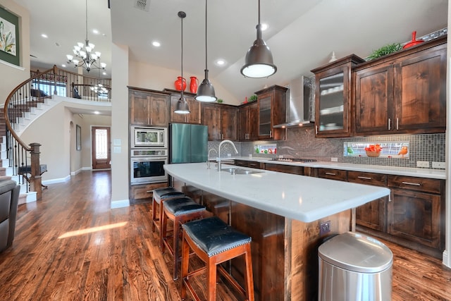 kitchen featuring light countertops, stainless steel appliances, dark wood-type flooring, a sink, and wall chimney range hood