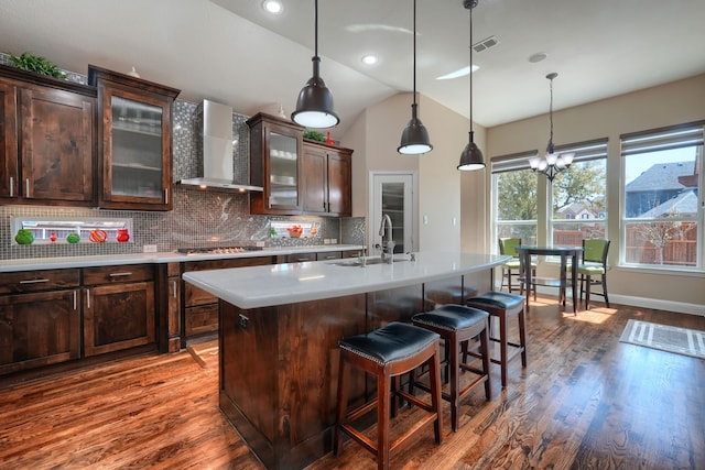 kitchen featuring vaulted ceiling, light countertops, a sink, wall chimney exhaust hood, and visible vents