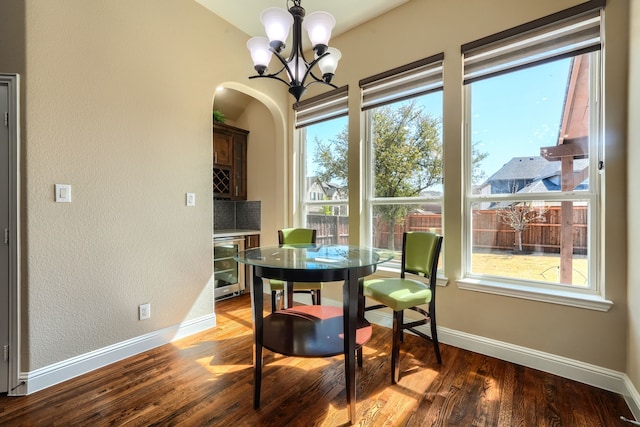 dining area featuring baseboards, arched walkways, wood finished floors, and an inviting chandelier
