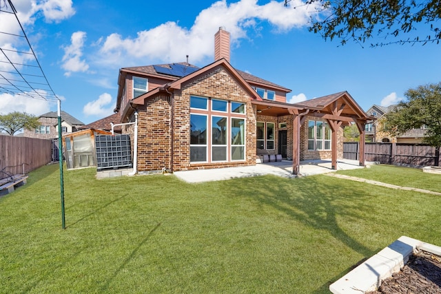 rear view of property with a fenced backyard, solar panels, a patio area, and brick siding