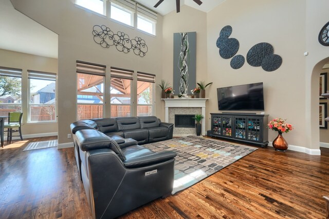 living area featuring arched walkways, ceiling fan, a glass covered fireplace, and wood finished floors