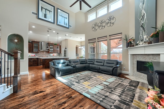 living area with a ceiling fan, a fireplace with flush hearth, dark wood-style floors, baseboards, and visible vents