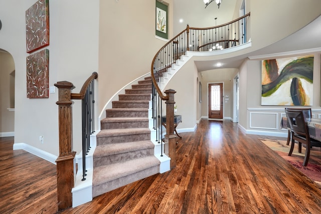 foyer with arched walkways, baseboards, wood finished floors, and stairway