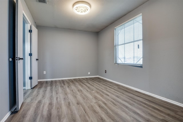 empty room featuring baseboards, visible vents, and wood finished floors