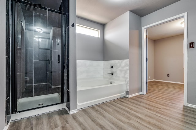 full bath featuring a stall shower, baseboards, wood finished floors, and a garden tub