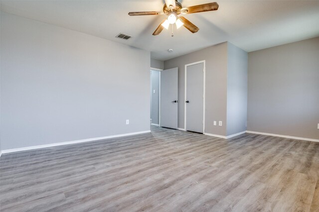 unfurnished bedroom with wood finished floors, baseboards, ceiling fan, and visible vents