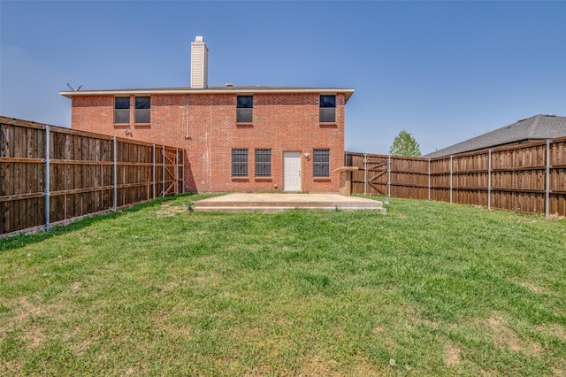 back of house featuring a lawn, a fenced backyard, a patio area, brick siding, and a chimney