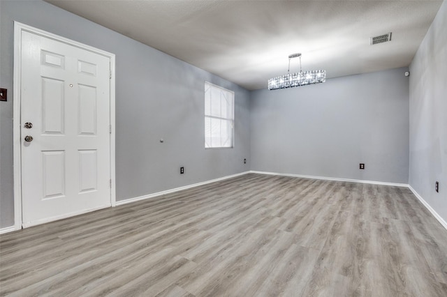 unfurnished room featuring baseboards, light wood-type flooring, visible vents, and a notable chandelier