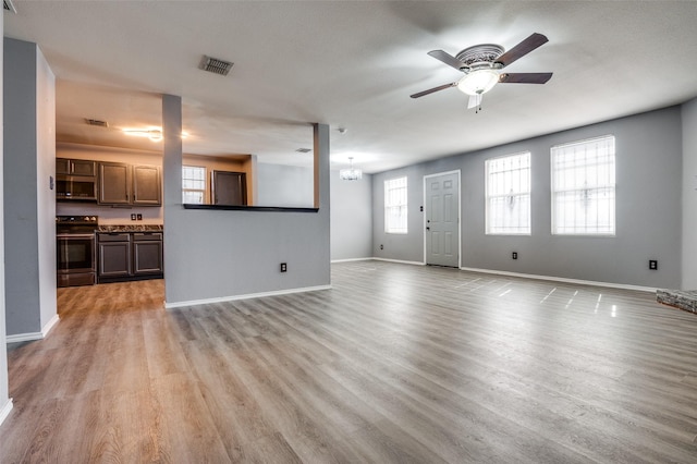 unfurnished living room featuring ceiling fan with notable chandelier, visible vents, light wood-style floors, and baseboards