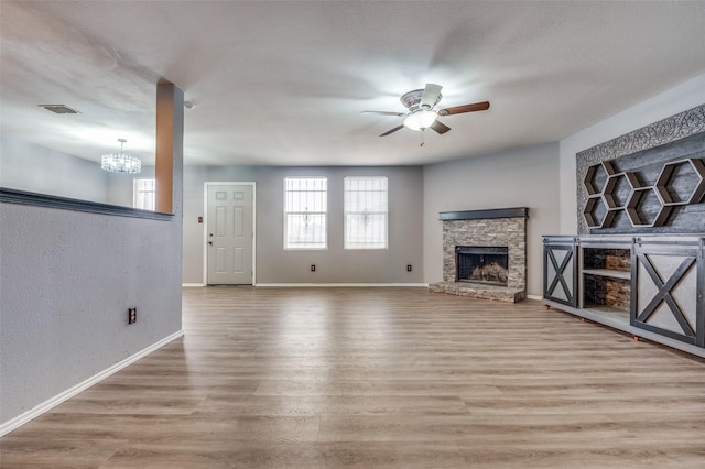 unfurnished living room with ceiling fan with notable chandelier, a fireplace, wood finished floors, and baseboards
