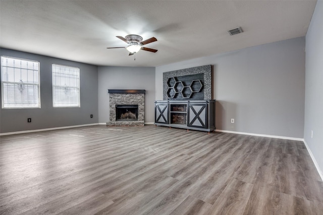 unfurnished living room featuring visible vents, baseboards, ceiling fan, wood finished floors, and a stone fireplace