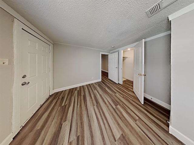 unfurnished bedroom featuring wood finished floors, visible vents, baseboards, a textured ceiling, and a walk in closet