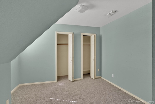 unfurnished bedroom with visible vents, baseboards, multiple closets, vaulted ceiling, and carpet flooring