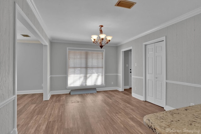 unfurnished dining area featuring a chandelier, visible vents, ornamental molding, and wood finished floors