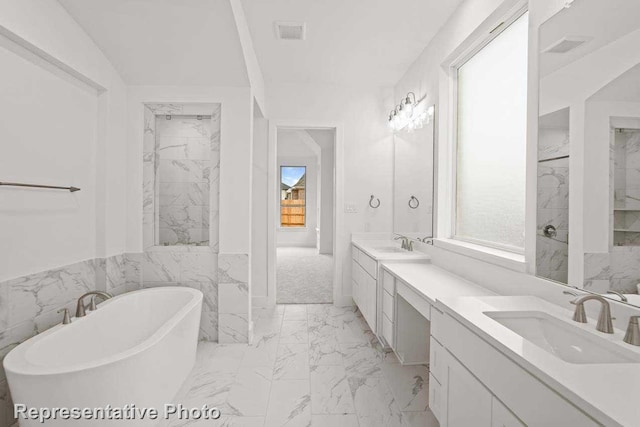 full bath with a healthy amount of sunlight, double vanity, a freestanding tub, marble finish floor, and a sink