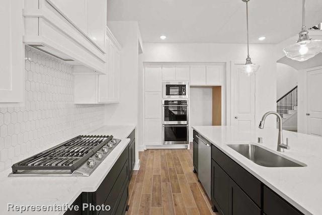 kitchen with dark cabinetry, a sink, white cabinets, appliances with stainless steel finishes, and tasteful backsplash