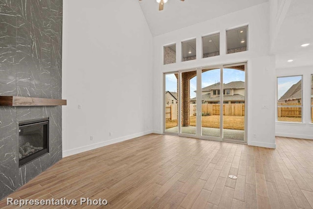 unfurnished living room with baseboards, a fireplace, wood finished floors, high vaulted ceiling, and a ceiling fan