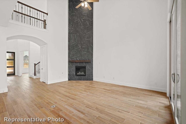 unfurnished living room with ceiling fan, a premium fireplace, a high ceiling, wood finished floors, and arched walkways