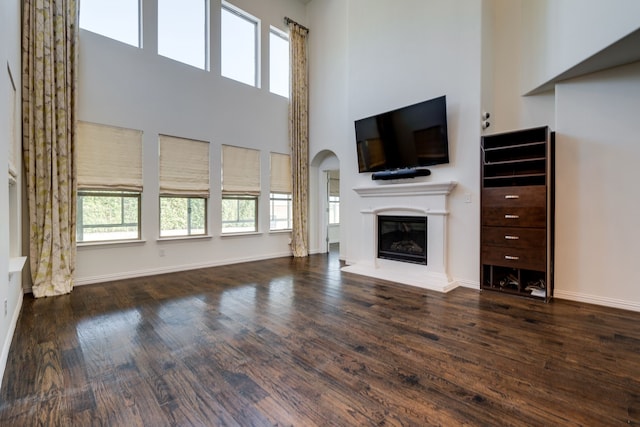 unfurnished living room featuring a high ceiling, wood finished floors, baseboards, and a glass covered fireplace