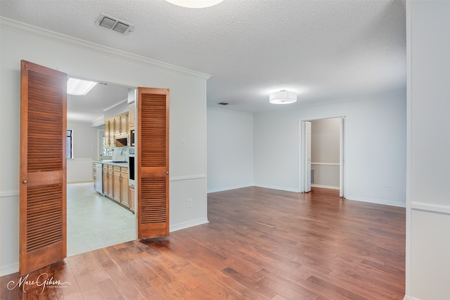 empty room featuring a textured ceiling, visible vents, ornamental molding, and wood finished floors