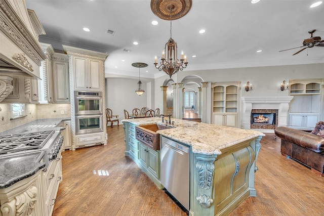 2909 Canyon Creek Dr, Sherman, TX 75092 - kitchen with cream cabinetry, appliances with stainless steel finishes, open floor plan, a ceiling fan, and a warm lit fireplace