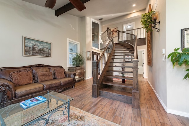 living area with ceiling fan, a towering ceiling, wood finished floors, stairs, and baseboards