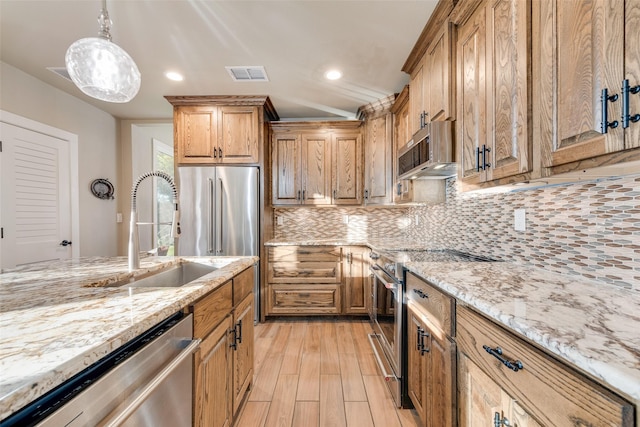 kitchen with appliances with stainless steel finishes, light stone counters, visible vents, decorative backsplash, and a sink