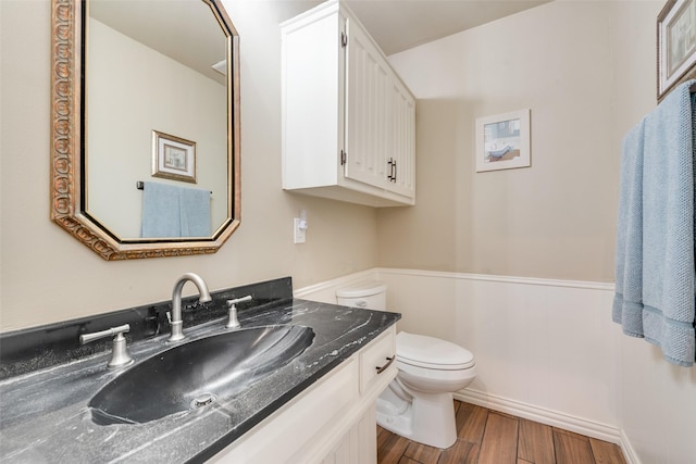 half bathroom featuring toilet, wainscoting, vanity, and wood finished floors