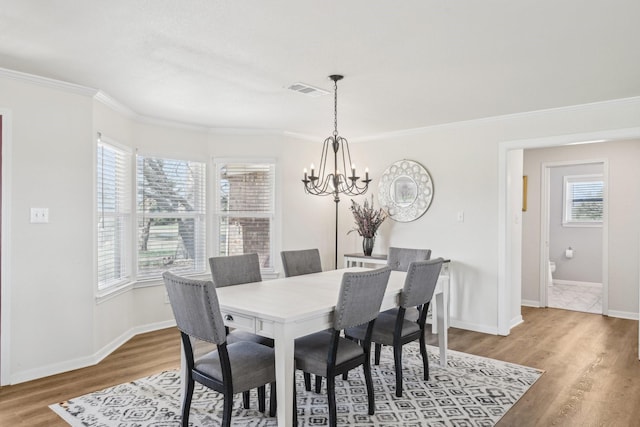 dining room with wood finished floors, baseboards, visible vents, ornamental molding, and an inviting chandelier