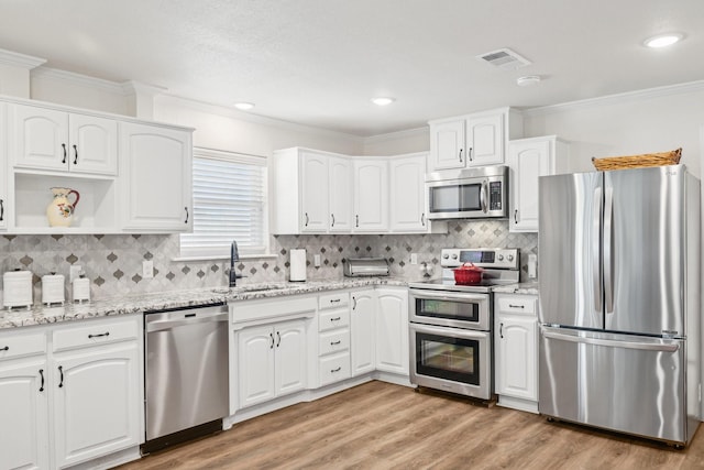 kitchen with crown molding, stainless steel appliances, a sink, light wood finished floors, and visible vents