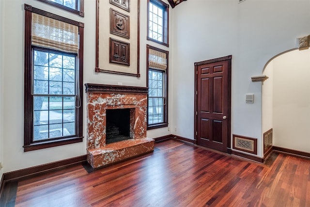 unfurnished living room with arched walkways, baseboards, dark wood finished floors, and a high end fireplace