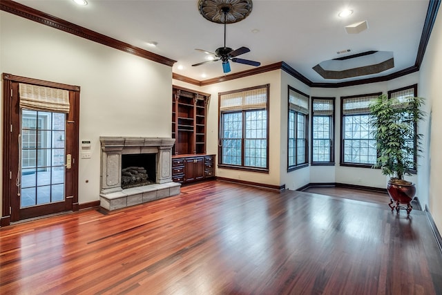 unfurnished living room with ceiling fan, a fireplace, wood finished floors, baseboards, and ornamental molding