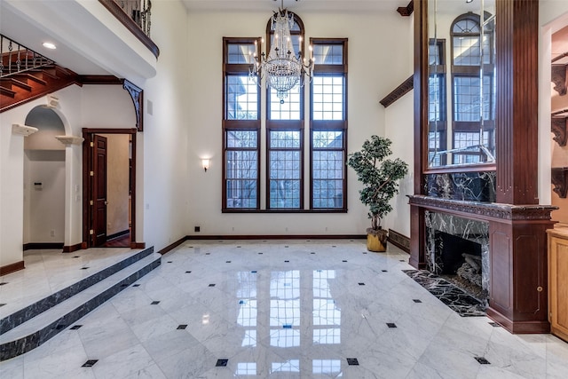 foyer featuring baseboards, a high ceiling, ornate columns, and a notable chandelier