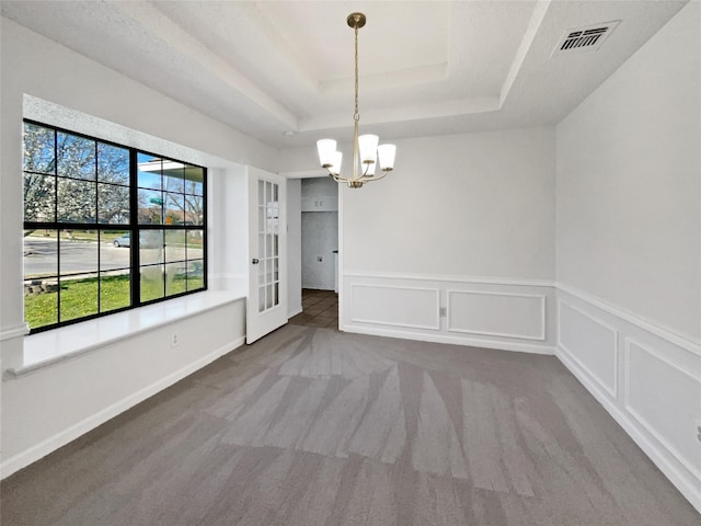 unfurnished dining area featuring visible vents, a chandelier, carpet flooring, a decorative wall, and a raised ceiling