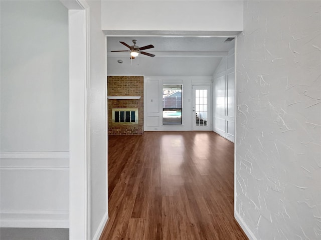 unfurnished living room featuring ceiling fan, dark wood-type flooring, a textured ceiling, a brick fireplace, and a textured wall