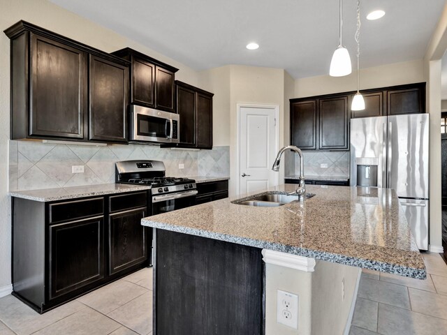 kitchen featuring decorative light fixtures, a center island with sink, a sink, light stone countertops, and appliances with stainless steel finishes