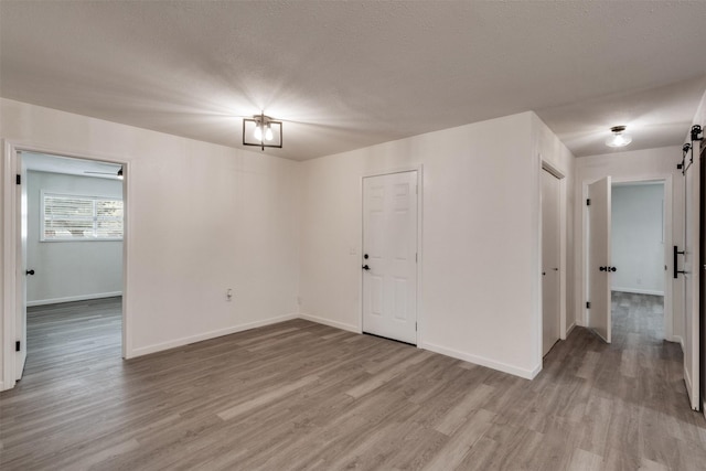 411 N 5th Ave, Munday, TX 76371 - spare room with a barn door, baseboards, a textured ceiling, and light wood-style flooring