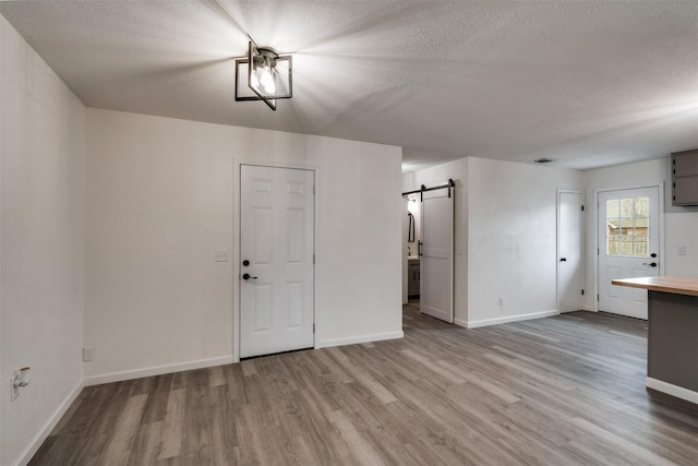 411 N 5th Ave, Munday, TX 76371 - unfurnished living room featuring a barn door, baseboards, a textured ceiling, and wood finished floors