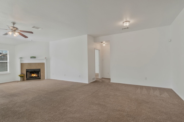 unfurnished living room with a tiled fireplace, a ceiling fan, visible vents, and carpet floors