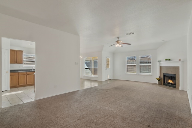 unfurnished living room featuring light tile patterned floors, a ceiling fan, visible vents, a fireplace, and light carpet