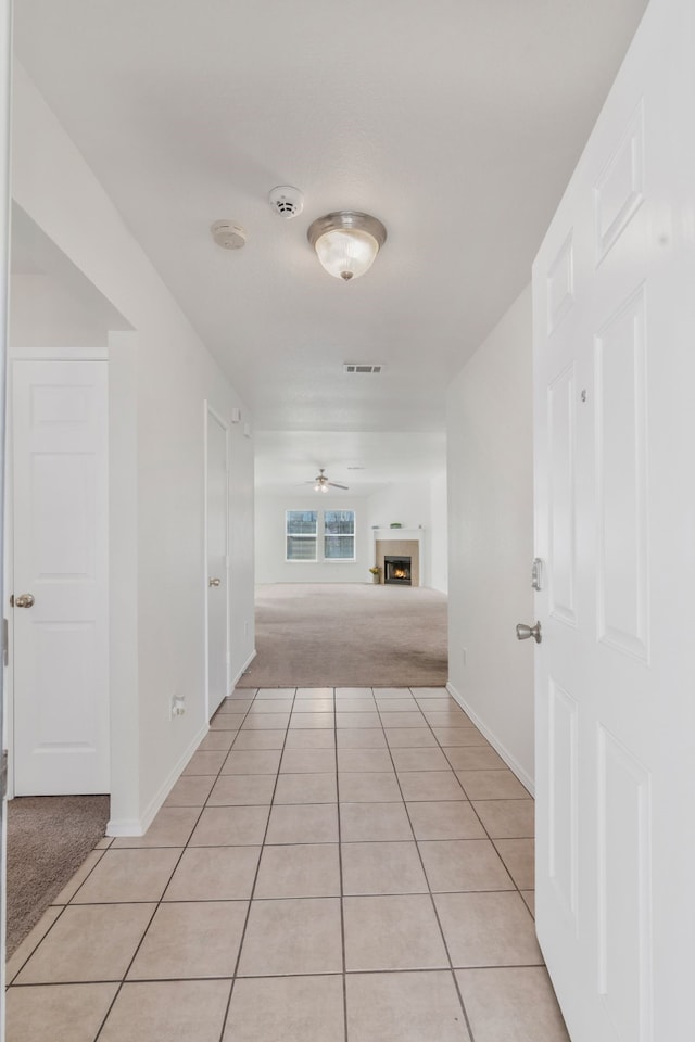 hallway with light carpet, light tile patterned floors, baseboards, and visible vents