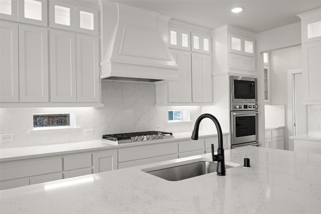 7127 Seagrove Ct, Grand Prairie, TX 75054 - kitchen with appliances with stainless steel finishes, premium range hood, white cabinetry, tasteful backsplash, and light stone counters