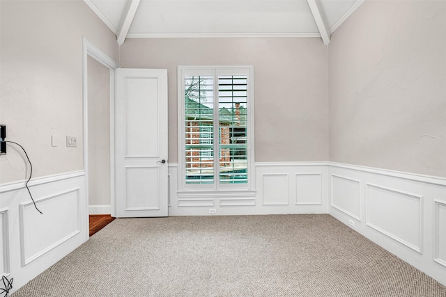carpeted spare room featuring lofted ceiling, a decorative wall, wainscoting, and ornamental molding
