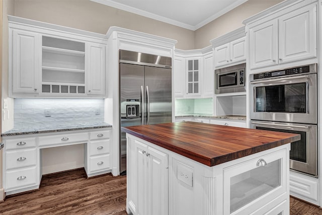 kitchen with built in appliances, white cabinets, butcher block counters, and crown molding