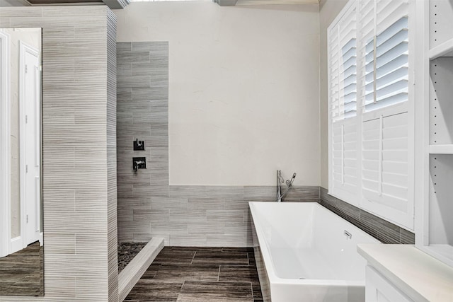 bathroom with wood finish floors, a freestanding tub, and tile walls
