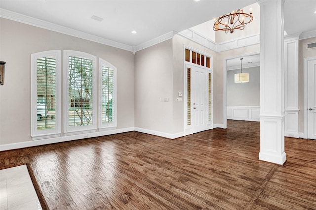 foyer entrance with visible vents, wood finished floors, crown molding, a chandelier, and ornate columns