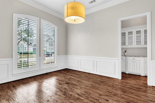 unfurnished dining area with crown molding, dark wood-style floors, visible vents, and wainscoting