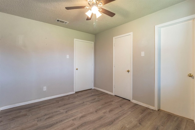 unfurnished bedroom featuring visible vents, baseboards, wood finished floors, a textured ceiling, and a ceiling fan